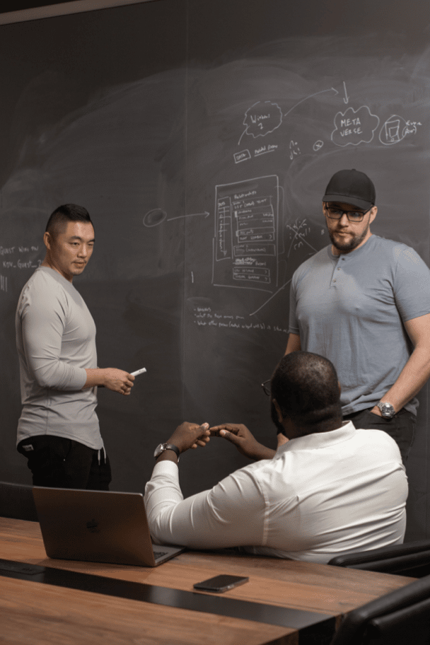 Men discussing market strategy in front of a blackboard with a laptop.